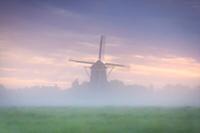 Hollands polderlandschap met molen tijdens een mistige zonsopkomst